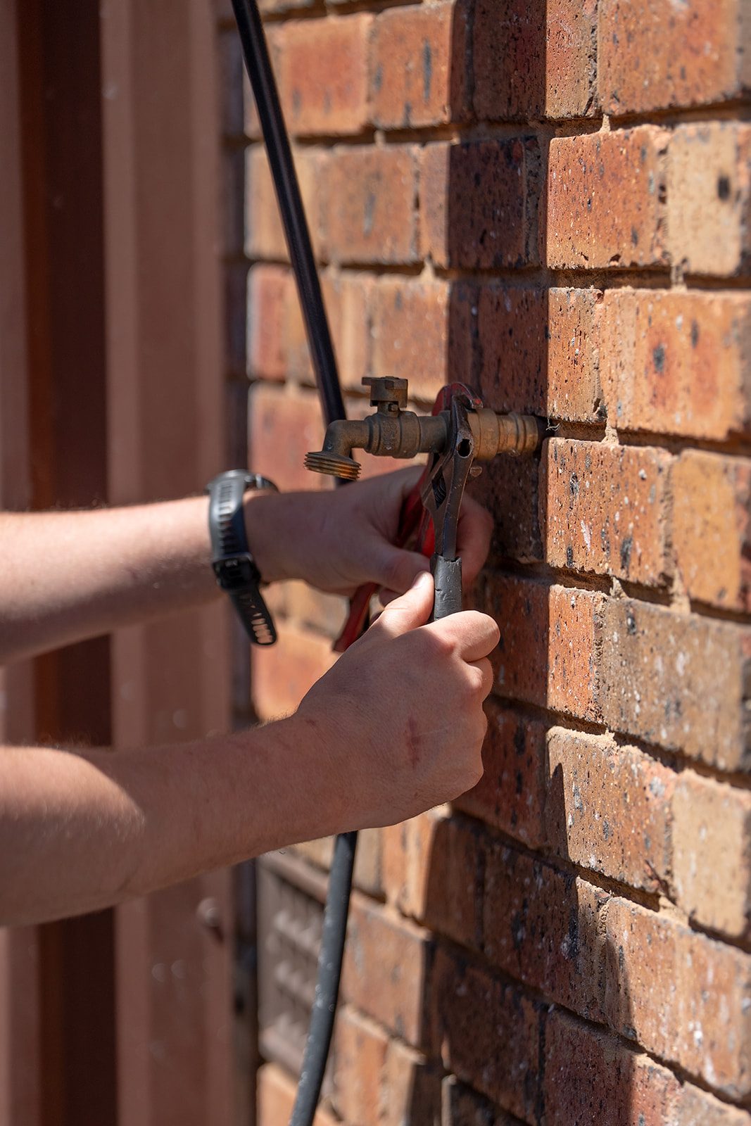 Hands on an outdoor tap at a brick wall